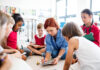 A group of small school kids with teacher sitting on the floor in class, learning