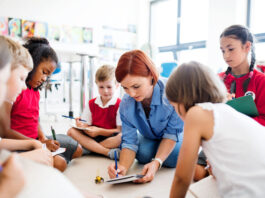 A group of small school kids with teacher sitting on the floor in class, learning