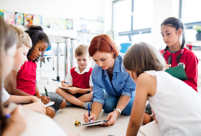 A group of small school kids with teacher sitting on the floor in class, learning