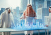 Business Developers in Traditional Clothes Discuss Investing Opportunities Based on Holographic Augmented Reality 3D City Model in Their Modern Office in a Skyscraper.