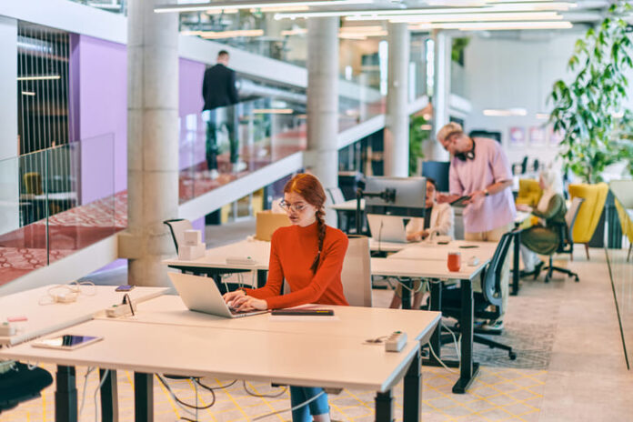 professional businesswoman with orange hair sitting at her laptop, epitomizing innovation and productivity in her contemporary workspace