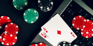 Red And Black Casino Chips On A Table With A Laptop And Playing Cards