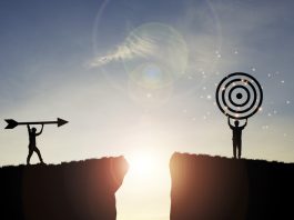 Silhouette men throwing arrow and holding dartboard on mountain with blue sky and sunlight for achievement objectives target