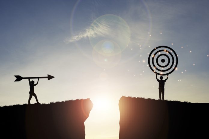 Silhouette men throwing arrow and holding dartboard on mountain with blue sky and sunlight for achievement objectives target