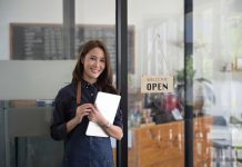 Smiling female waitress holding digital tablet and standing in modern coffee shop