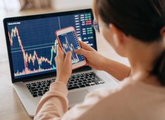 Woman crypto trader investor broker using smartphone app and laptop executing financial stock trade market trading order to buy or sell cryptocurrency