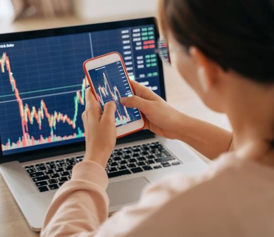 Woman crypto trader investor broker using smartphone app and laptop executing financial stock trade market trading order to buy or sell cryptocurrency