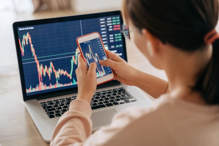 Woman crypto trader investor broker using smartphone app and laptop executing financial stock trade market trading order to buy or sell cryptocurrency