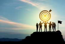 Silhouettes of group businessmen holding target boards with flags planted on a mountain.