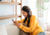 Woman texting messages relaxing on couch in cozy living room at home