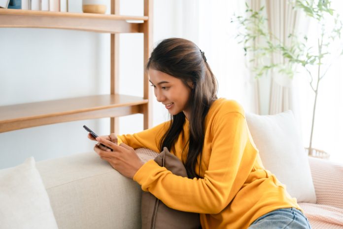 Woman texting messages relaxing on couch in cozy living room at home