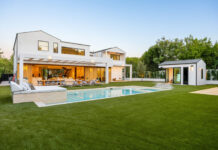 Modern luxury home with a pool and spacious backyard featuring lush green lawn and elegant architecture under a clear sky.