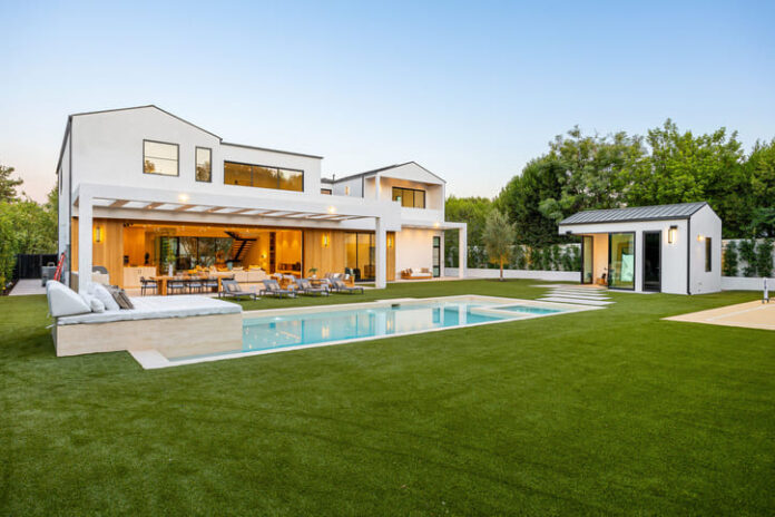 Modern luxury home with a pool and spacious backyard featuring lush green lawn and elegant architecture under a clear sky.