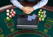 Close up of poker player with playing cards, laptop, chips at green casino table