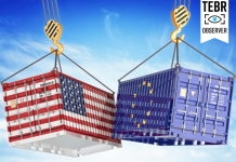 cargo containers with USA and European Union flags hoisted by crane hooks on blue cloudy sky