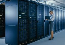 Female IT Technician Stands Near Rack Cabinet and Runs Maintenance Program on Laptop, Controls Operational Server's Optimal Functioning.