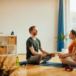 Young couple in lotus pose practicing Yoga together at home.