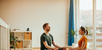 Young couple in lotus pose practicing Yoga together at home.