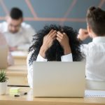 Frustrated african-american woman feeling burnout in shared office with laptop