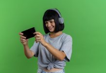 Smiling young brunette caucasian woman on headphones holds and looks at phone