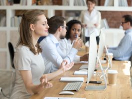 Peaceful millennial woman practice yoga in front of computer at workplace, calm female employee meditating controlling emotions and managing stress, worker sit in lotus position in office