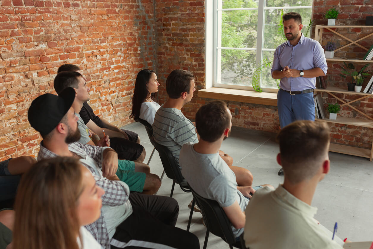 A man presents to a group of people seated in a room, discussing an enterprise search engine.