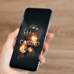 In the hands of a smartphone with playing cards the inscription casino, black-gold background.