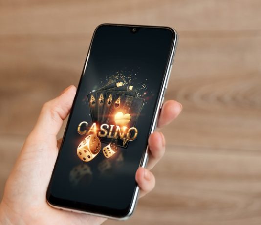 In the hands of a smartphone with playing cards the inscription casino, black-gold background.