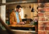 Handsome Man Typing on Laptop Computer in Loft Apartment, Sunny Day Outside. Creative Male Checking Social Media, Browsing Internet. Productivity in Working From Home.