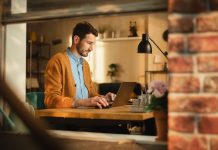 Handsome Man Typing on Laptop Computer in Loft Apartment, Sunny Day Outside. Creative Male Checking Social Media, Browsing Internet. Productivity in Working From Home.