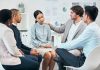 Diverse colleagues support and comfort unhappy, sad, emotional well-being coworker at team meeting or gathering. Compassionate, caring employees showing empathy to distressed woman