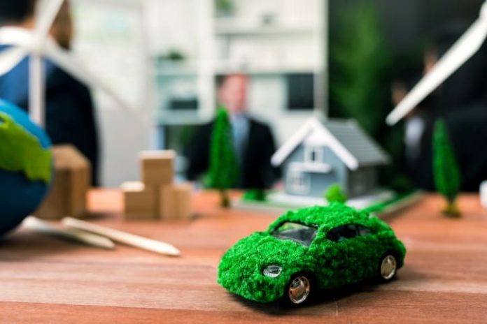 EV car model on table with blurred business people planning business marketing for eco-friendly car in background. Greener future with alternative energy charge utilization in business