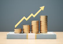 Yellow bullish arrow indicator bar chart design with stacks of coins stacked on top of 100 dollar bill on wooden background. money rise for Investor