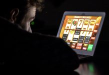 Gambling addicted man with glasses in front of online casino slot machine on laptop computer at night