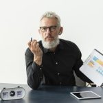 Older man at home showing graph on notepad with tablet on desk for traditional budgeting