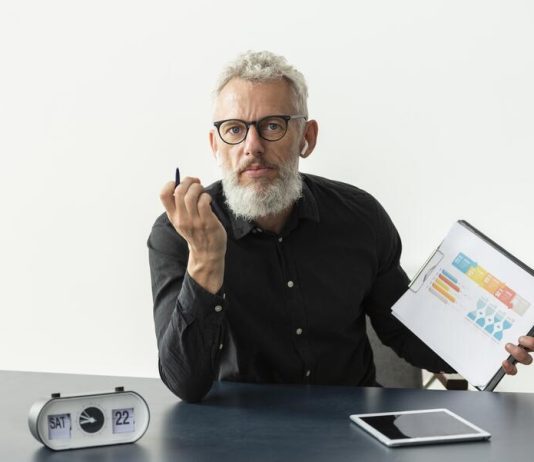 Older man at home showing graph on notepad with tablet on desk for traditional budgeting