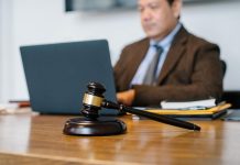 A male lawyer in a brown suit on his computer typing with a gavel front and center on his desk.